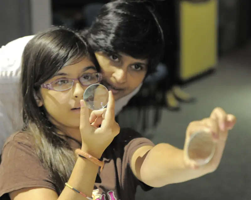 Two young students holding up glass lenses to see how they bend light