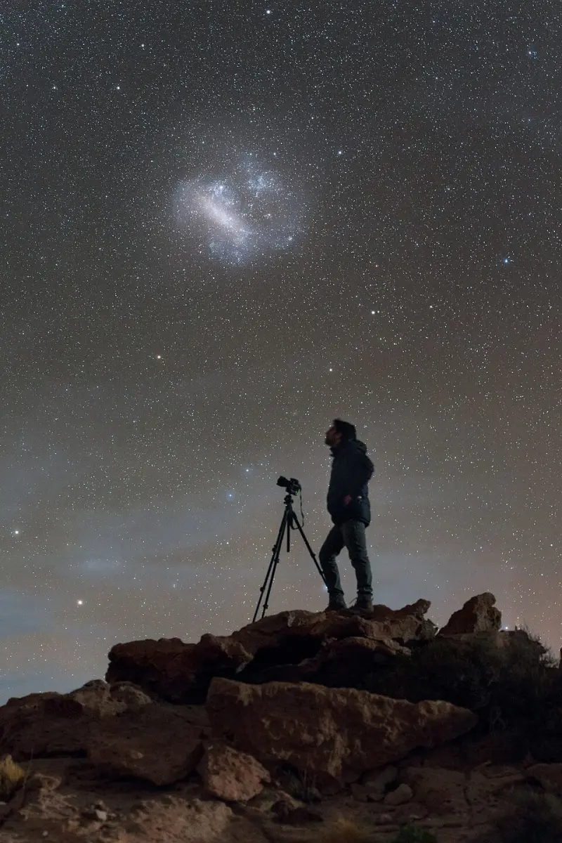 A stargazer with a camera on a tripod, standing under the Milky Way
