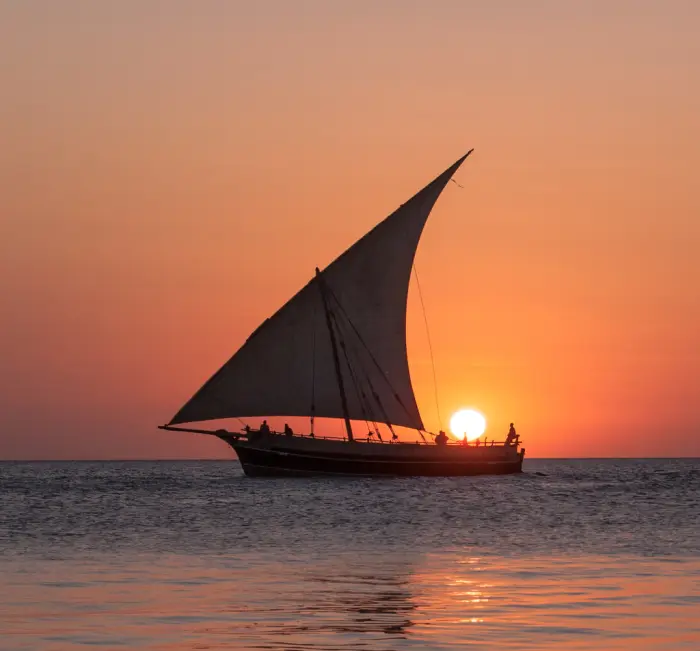 A dhow under sail with the sun setting directly behind it