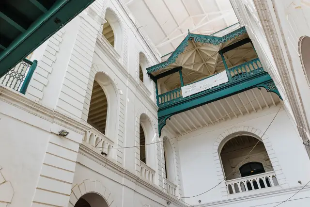 White arched galleries and a green carved timber balcony around a courtyard, seen from below