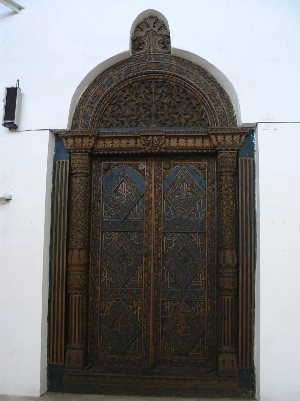 A carved Zanzibari door in dark teak with an arched lintel of carved vines, set into a white limewashed wall
