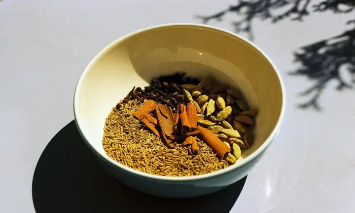 Cloves, cinnamon sticks, cardamom and cumin in a white bowl