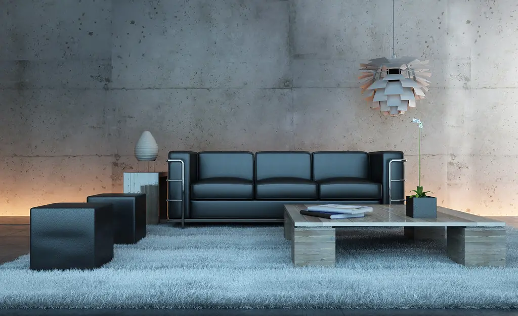 A black leather sofa against a concrete wall, lit by a warm pendant and a glow along the floor