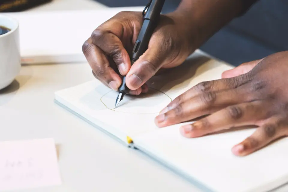 Hands sketching a first mark in a notebook with a fountain pen
