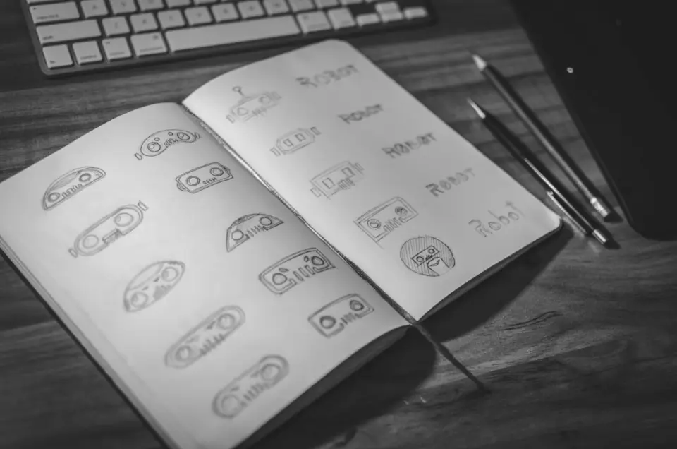 An open sketchbook filled with pencil logo explorations beside a keyboard