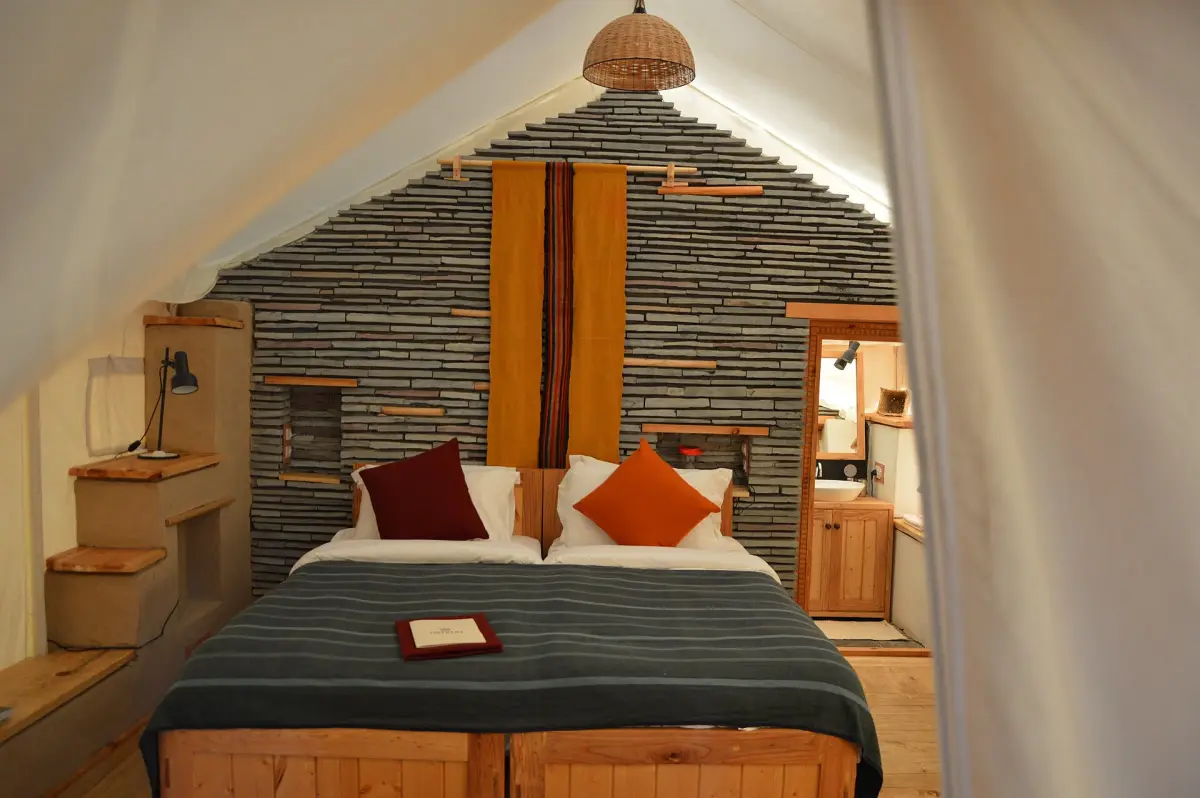Inside a Kopje Suite: a wide bed with rust cushions against a dry-stone wall, under canvas