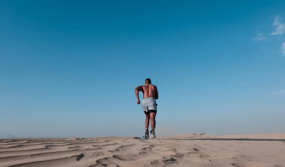 A lone man walking across desert dunes under a deep blue sky