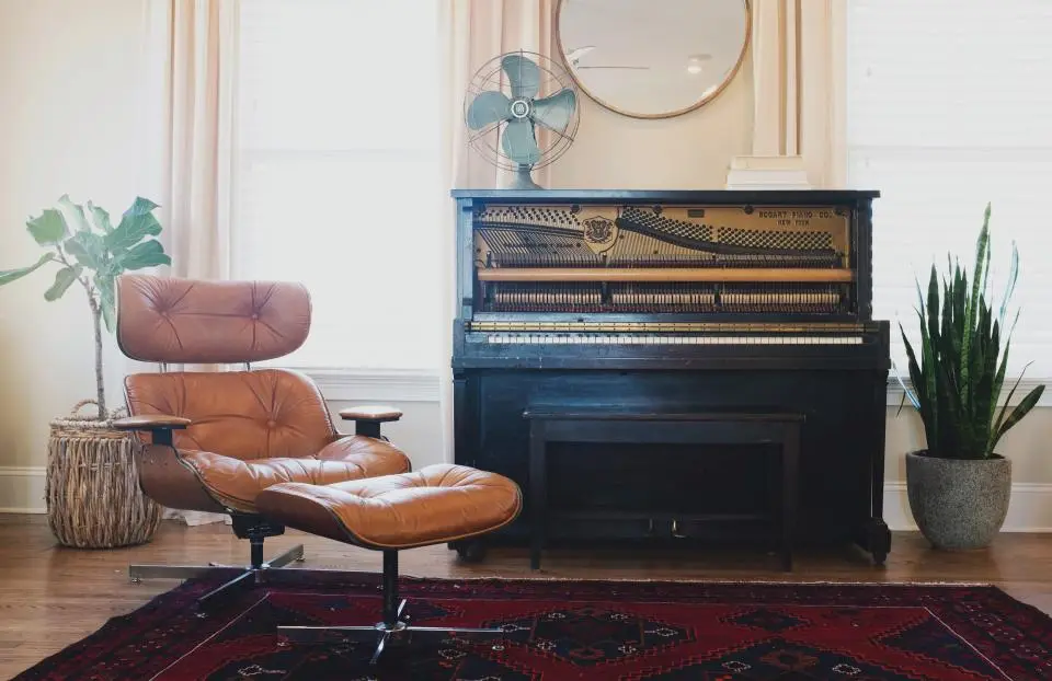 A leather lounge chair beside an upright piano and potted plants