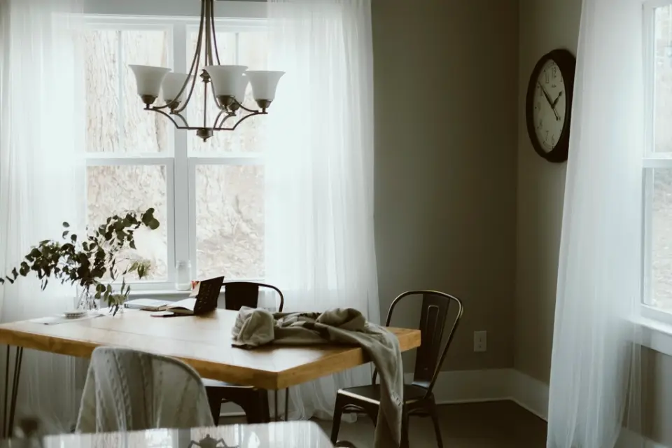 A dining table under a chandelier beside tall sheer curtains