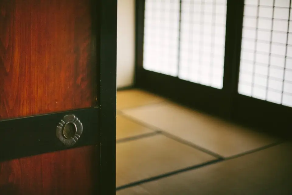 A timber door with a brass ring pull opening onto a calm room