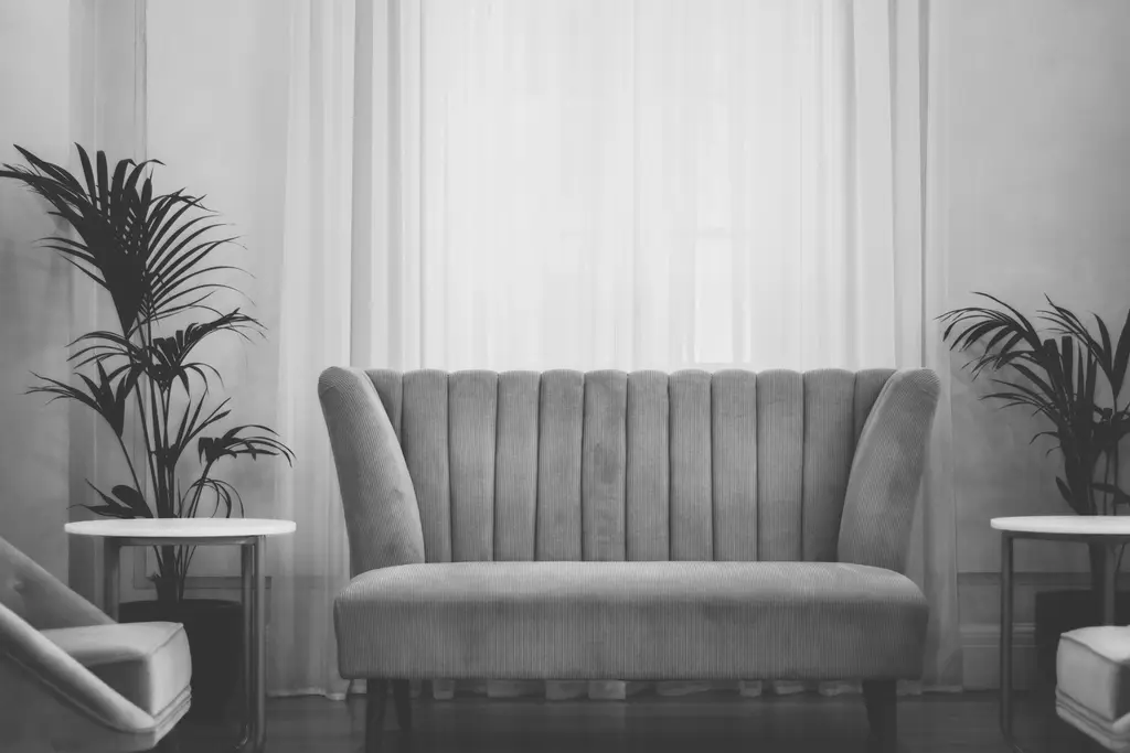A channel-tufted sofa between two palms and pale curtains, toned in deep green