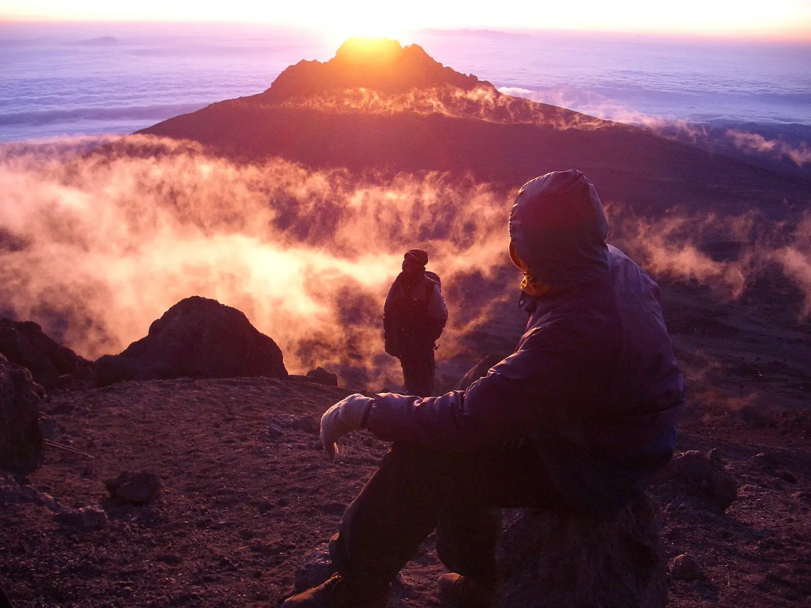 Climbers resting at first light high on Kilimanjaro, with Mawenzi peak above a sea of cloud