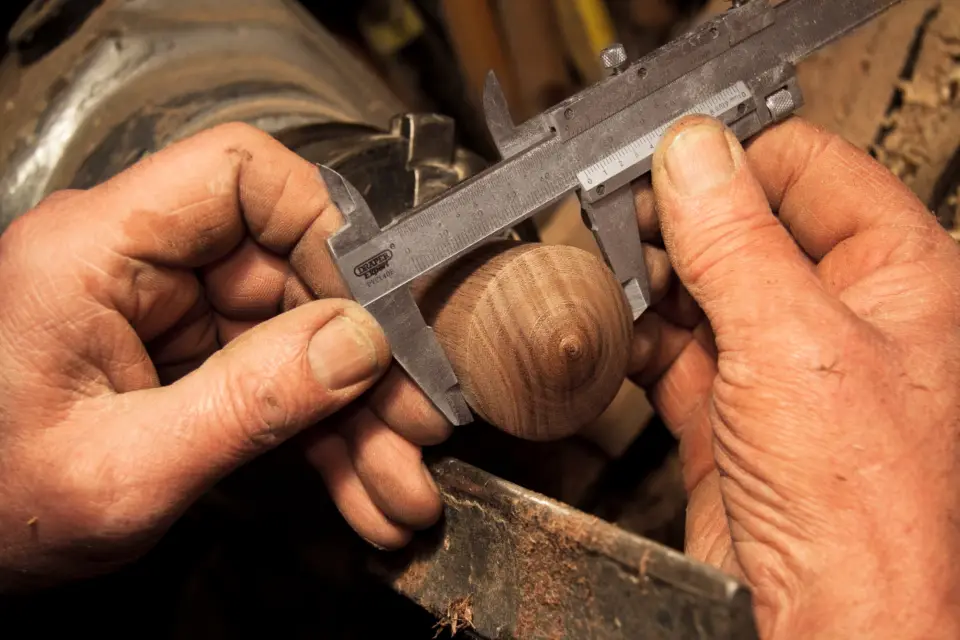 A carpenter's hands measuring a turned piece of wood with calipers