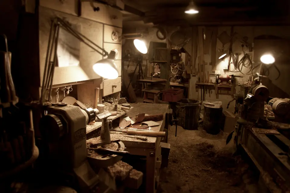A warm workshop with lamps over benches, tools and timber offcuts
