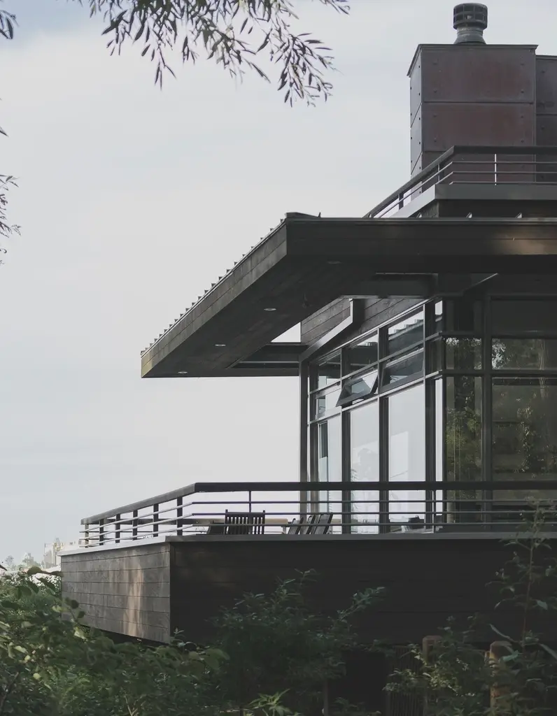 A glass-walled modern building with a deep cantilevered terrace among trees