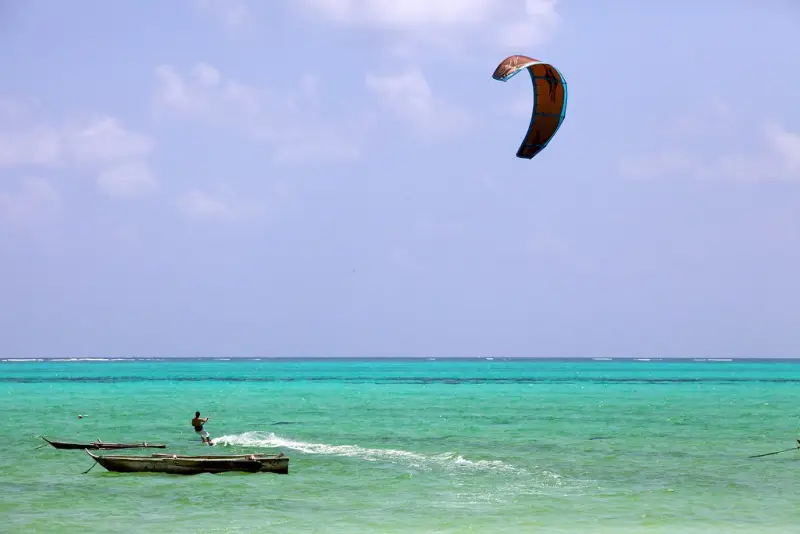 A kitesurfer crossing a turquoise lagoon past a moored boat